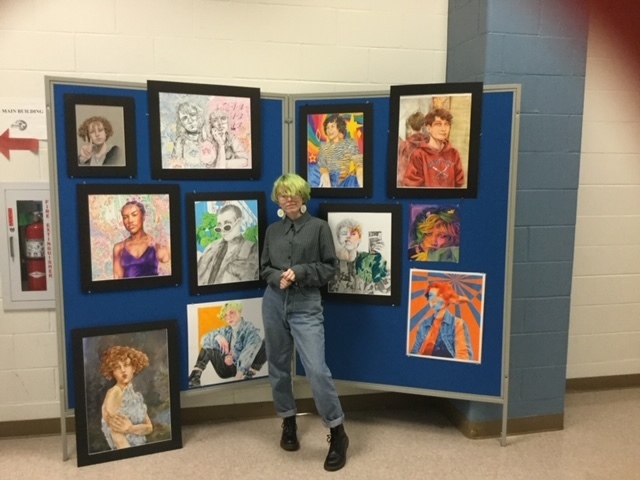 Mary Miller standing in front of her various art pieces displayed on a wall